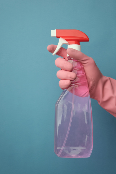 The cleaning agent in the spray gun is held with a hand in a blue rubber glove on a blue background